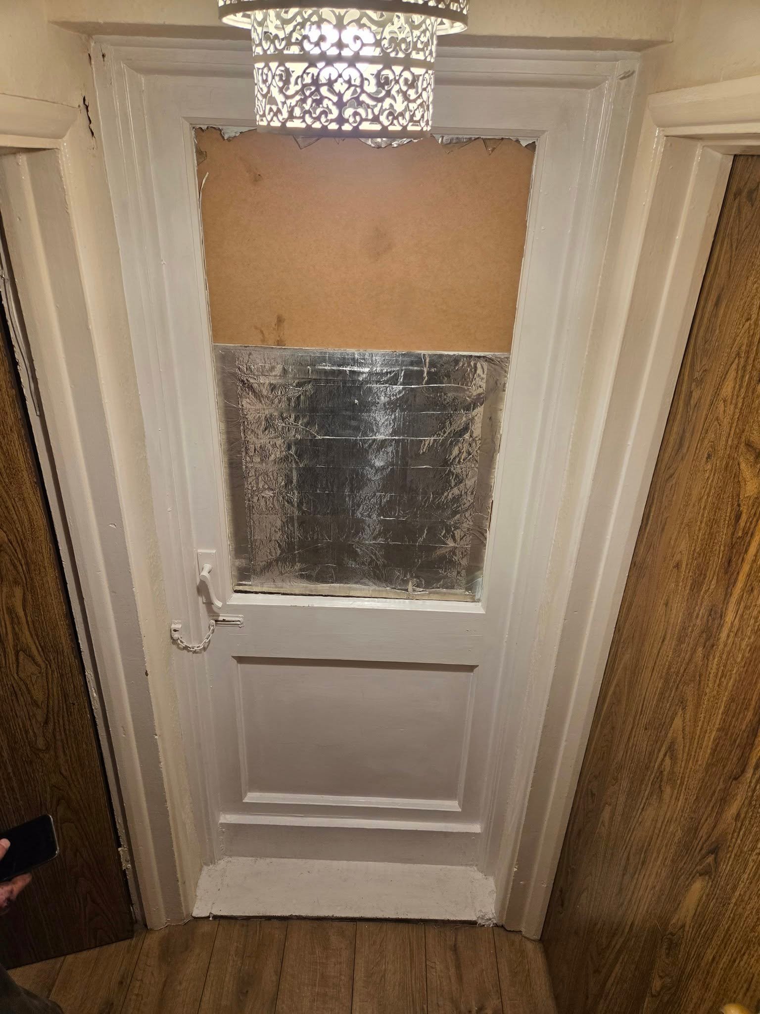 A front door with the window covered after a smash
